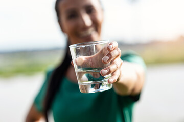Sporty young woman drinking water glass in the park.