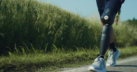Athletic Person With Disability Walking on the Side of The Road. A man With Bionic Limb Prosthesis Calmly Strolls While Recovering After Morning Run. Close Up on Legs, Slow Motion Shot. - Powered by Adobe