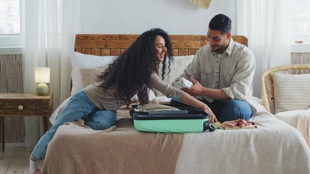 Hispanic married couple Indian newlyweds spouses husband and wife boyfriend and girlfriend curly woman and bearded man getting ready to trip honeymoon after wedding in bedroom put clothing in suitcase