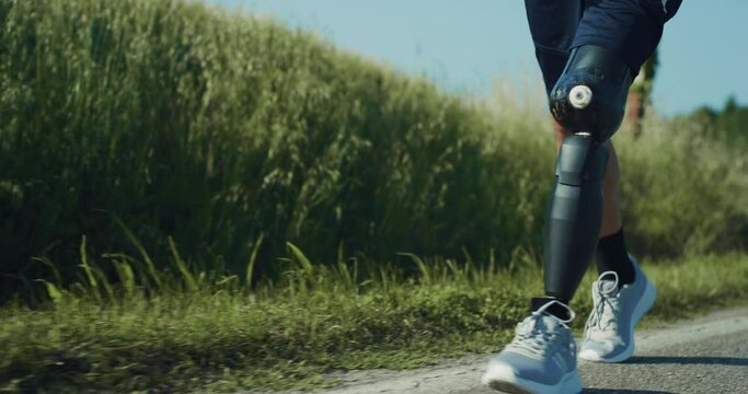 Athletic Person With Disability Walking on the Side of The Road. A man With Bionic Limb Prosthesis Calmly Strolls While Recovering After Morning Run. Close Up on Legs, Slow Motion Shot.