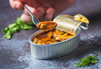 Hand with a fork pricking canned pickled mussels on a dark blue table with pasrley