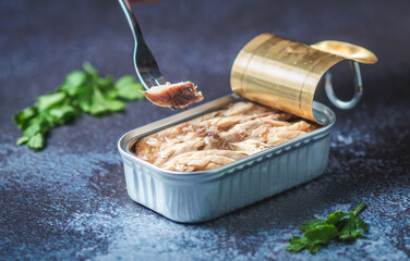 Fork pricking canned mackerel on a dark blue table with parsley. Ready for eat.