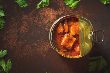Canned octopus with american sauce open on a dark brown table with parsley. Ready for eat. 