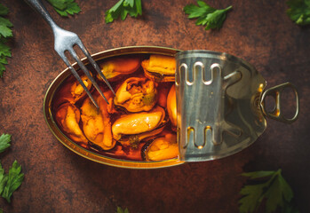 Canned pickled mussels open on a dark brown table with a fork and parsley. Ready for eat. 