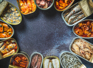 Preserve cans with different products, fish and seafood, natural or pickled, open on a dark table. Ready to eat.