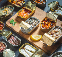 Preserve cans with different products, fish and seafood, natural or pickled, open on a dark table...