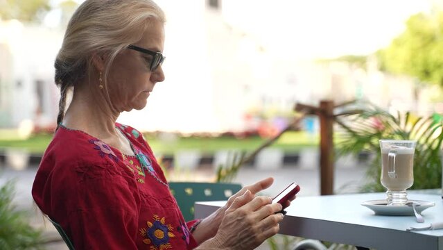 Profile view of mature elderly woman wearing ethnic clothes texting friends and family while on vacation sitting at a cafe.