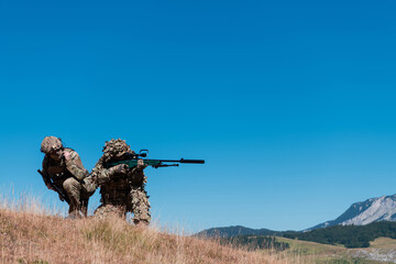 A sniper team squad of soldiers is going undercover. Sniper assistant and team leader walking and aiming in nature with yellow grass and blue sky. Tactical camouflage uniform.