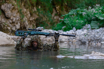 A military man or airsoft player in a camouflage suit sneaking the river and aims from a sniper...