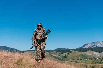 Army soldier holding a sniper rifle with scope and walking in the forest. war, army, technology and...