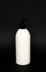White unbranded bottle with a black dispenser isolated on black background. cosmetic packaging mockup with copy space. Bottle for a shower, gel, soap.