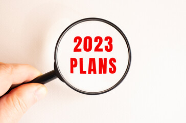 A man's hand holds a magnifying glass. Close-up of the 2023 PLANS text.
