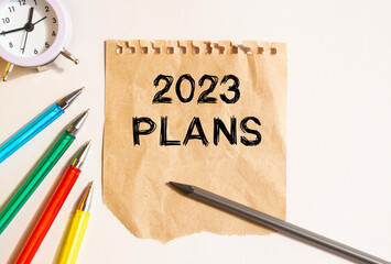 On the table lies a rumpled sheet of kraft paper torn from a notebook. Text on the 2023 PLANS sheet. Colored pens.