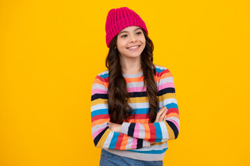 Beautiful teen girl in a winter hat and a warm sweater. A child on a yellow isolated background. Happy teenager, positive and smiling emotions of teen girl.