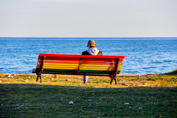 Naklejka na ściany i meble person seated on colorful bench enjoying the sea
