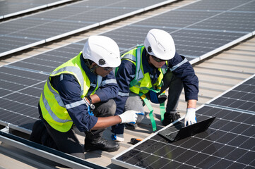 Caucasian and African American engineer man use electric screwdriver and computer notebook working with solar panel on roof factory	