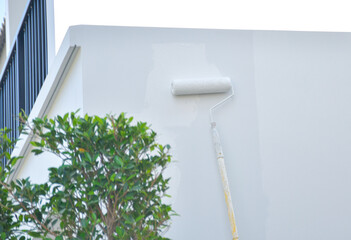 A worker is painting the walls of the house with a primer using a paint roller.