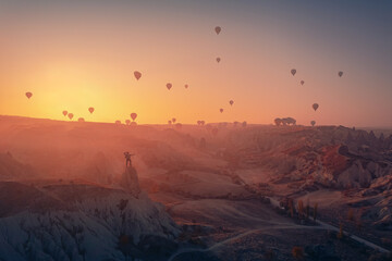 Hiker man in hat on top of mountain background hot air balloons Cappadocia Turkey. Amazing adventure photo from aerial drone view