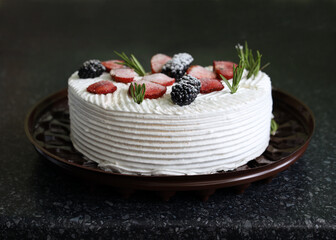 Cake with whipped cream and fruit. Biscuit cake with butter cream close-up. Delicious homemade birthday cake topped with rosemary sprigs, blackberries and strawberries. Delicious dessert for tea