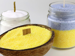 Yellow bulk candles in coconut with a wooden wick. Candles in a jar close-up. Making candles at home from palm oil. Bulk candles in different containers
