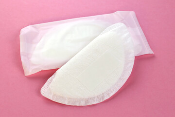 Two of sealed breast pads close up. disposable absorbent for preventing maternal milk dripping. A flat lay of white absorbent nursing pads on an pink background. Concept of natural breastfeeding.