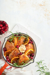 Baked chicken thighs with orange, cranberry and spicy herbs rosemary servered in frying pan on light background. Festive Christmas Dinner Concept menu. Top view. copy space