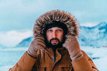 Headshot photo of a man in a cold snowy area wearing a thick brown winter jacket and gloves. Life...