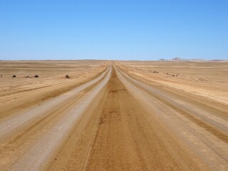Fototapeta na wymiar Empty desert road in the Namib-Nauluft park of Namibia, blue sky and no vegetation.