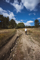 Obraz premium far away shot of landscape with Woman walking in a field carrying a basket of flowers in the rocky mountains - dirt road, foraging, sustainable lifestyle