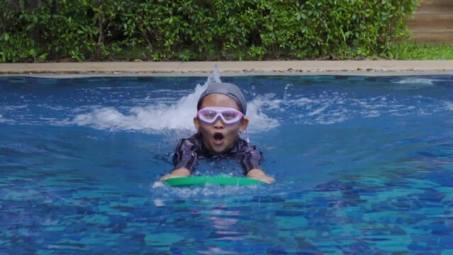 4K, Asian girl wearing black swimsuit and swimming cap, with swimming goggles, playing in children's pool, grabbed a swimming training board, keep his balance in water, fluently hit the legs in water.