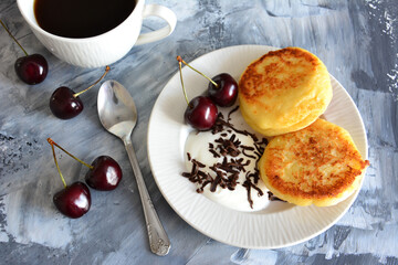 ukrainian syrniki with sour cream, cherries and cup of coffee isolated on concrete background