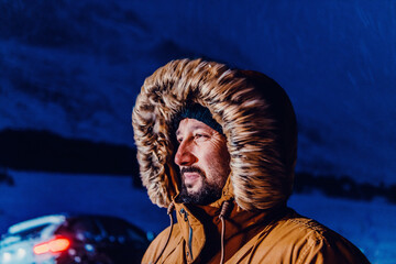 Head shot of a man in a cold snowy area wearing a thick brown winter jacket, snow goggles and...