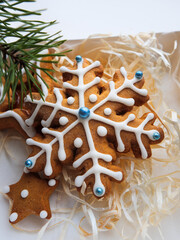Christmas gingerbread cookies lie in a white box with straw near a pine branch. christmas cookies with icing. cookie in the form of a snowflake with blue dots. gingerbread lies on a white table.