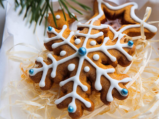 Christmas gingerbread cookies lie in a white box with straw near a pine branch. christmas cookies with icing. cookie in the form of a snowflake with blue dots. gingerbread lies on a white table.