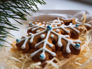Christmas gingerbread cookies lie in a white box with straw near a pine branch. christmas cookies with icing. cookie in the form of a snowflake with blue dots. gingerbread lies on a white table.