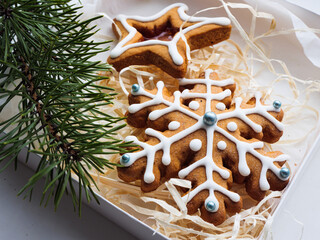 Christmas gingerbread cookies lie in a white box with straw near a pine branch. christmas cookies with icing. cookie in the form of a snowflake with blue dots. gingerbread lies on a white table.