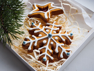 Christmas gingerbread cookies lie in a white box with straw near a pine branch. christmas cookies with icing. cookie in the form of a snowflake with blue dots. gingerbread lies on a white table.