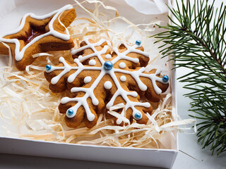 Christmas gingerbread cookies lie in a white box with straw near a pine branch. christmas cookies with icing. cookie in the form of a snowflake with blue dots. gingerbread lies on a white table.