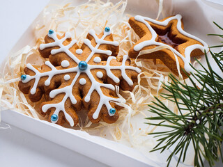 Christmas gingerbread cookies lie in a white box with straw near a pine branch. christmas cookies with icing. cookie in the form of a snowflake with blue dots. gingerbread lies on a white table.