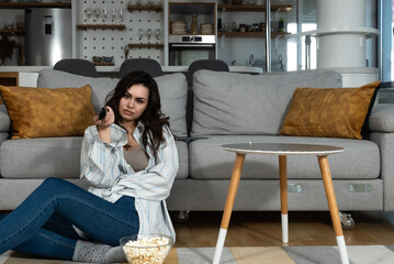 Young freelancer business woman bored by tv program sitting at home on day off dont know what to do. Casual female feel boredom at apartment during her sick days eating popcorns and watch television.