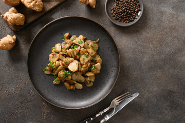 Fresh roasted Jerusalem artichoke root, sunchokes with garlic and parsley on brown background. View from above. Copy space.