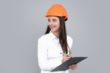 Young woman construction manager. Woman builder isolated portrait with protect helmet and clipboard. Gray background, copy space.