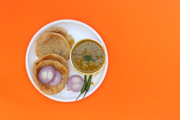 Top View of Flat Kachori or Kachodi in Plate  with Ghugni Pea Curry in Bowl, Green Chillies and Onion Slices Isolated on Yellow Background with Copy Space