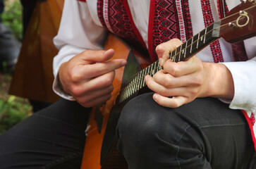 School boy in a white embroidered shirt and black trousers plays a musical instrument balalaika at...