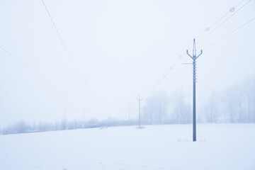 Power line in winter covered in frost and snow, foggy landscape