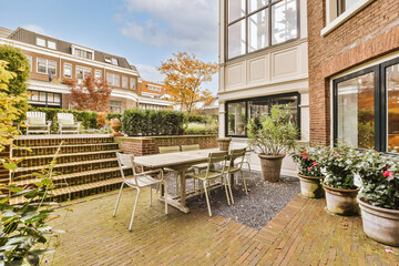 a patio area with chairs, tables and potted plants on the side of the house there is a brick wall...