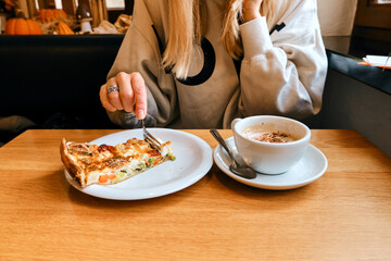 A woman with a cup of aromatic coffee and a cake sits in a cafe or restaurant. The girl drinks a hot latte or cappuccino after breakfast with a delicious dessert