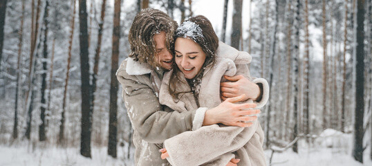 Love romantic young couple. Guy hugging kissing girl in snowy winter forest. Walking,having fun in trees, laughing. Stylish clothes,fur coat,jacket,woolen shawl. Snow lovestory. Romantic date,weekend