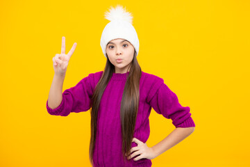 Modern teen girl wearing sweater and knitted hat on isolated yellow background.