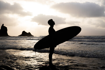 Silhuoette of a surfer at the beach during sunset looking at the sky.